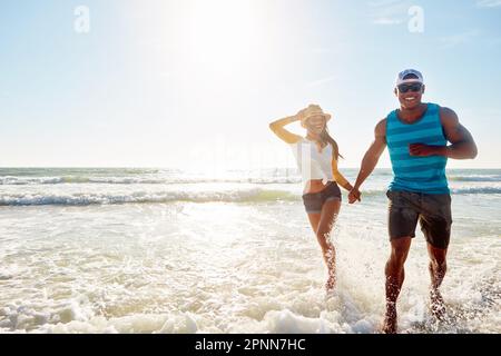 Scappare da tutto il resto tranne noi. una giovane coppia felice che fa una passeggiata sulla spiaggia. Foto Stock