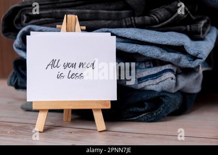 TUTTO CIÒ DI CUI HAI BISOGNO È MENO testo su carta nota su Jeans assortimento abbigliamento shopping sostenibile di seconda mano. Armadio a capsula minimal. Consumo eccessivo di moda sostenibile, consumo di acquisto cosciente, concetto di idea di modo lento. Stile di vita a basso contenuto di rifiuti Foto Stock