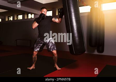Un giovane uomo adulto atletico sta effettuando un workout ad alta intensità usando una borsa di boxing Foto Stock
