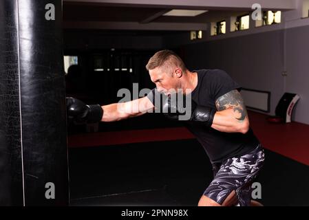 Un giovane uomo adulto atletico sta effettuando un workout ad alta intensità usando una borsa di boxing Foto Stock