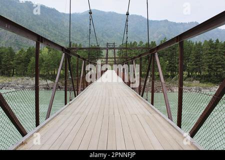 terrazze in legno su un ponte sospeso in ferro per pedoni che attraversano il fiume. Foto Stock