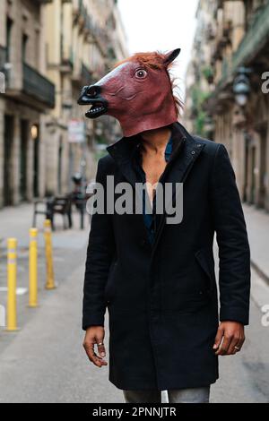 Uomo elegante che indossa una maschera a cavallo mentre si è in piedi all'aperto per strada. Foto Stock