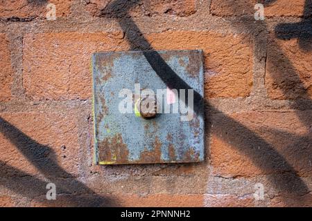 piastra di fissaggio in ferro e acciaio e bullone in una parete di mattoni rossi con ombre e luce solare Foto Stock