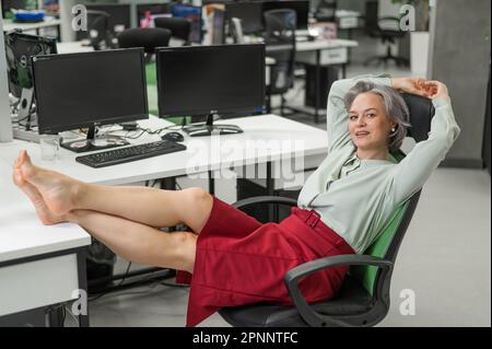 Donna caucasica matura tolse le scarpe e mise i piedi sul desktop in ufficio. Foto Stock