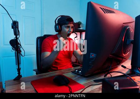 Euforico giovane streamer latino-americano che celebra una vittoria. Concetto di videogamer online e videogiochi. Foto Stock