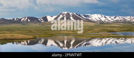 Kirghizistan natura verde paesaggio con un lago riflesso e vaste montagne. Il Kirghizistan è un paese senza sbocco sul mare situato nell'Asia centrale, noto per la sua Foto Stock