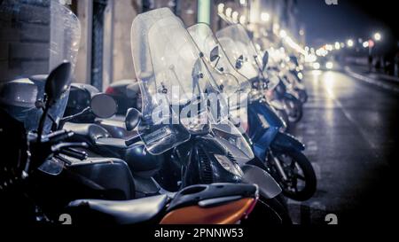 Lucca, Italia - Dicembre 2022: Moto scooter parcheggiate l'una accanto all'altra di notte su una strada può essere una vista comune in aree urbane dove scooter-sh Foto Stock