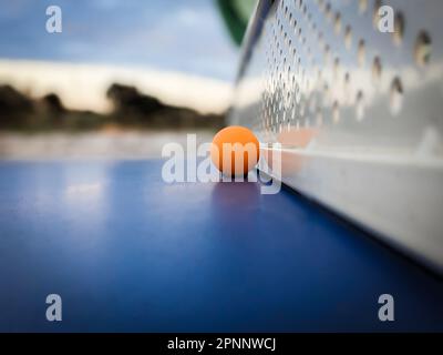 Un vibrante pallina da ping pong arancione su un tavolo blu Foto Stock
