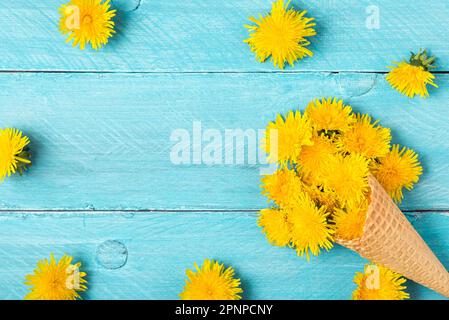 Composizione floreale. Cornice in fiori di dente di leone giallo con cono gelato su sfondo blu pastello. Disposizione creativa per le vacanze primaverili. Giacitura piatta Foto Stock