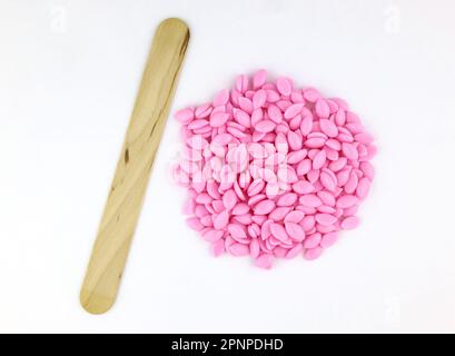 Bellissimi granuli di cera depilatoria rosa e spatole di legno su sfondo bianco. Epilazione, depilazione, rimozione dei peli superflui. Cera dura rosa perla BE Foto Stock