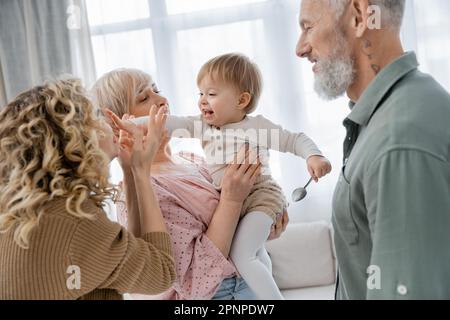 bambino spensierato che tocca faccia della madre vicino ai nonni felici nel paese, immagine di riserva Foto Stock