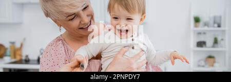 donna sorridente abbracciando nonna spensierata in cucina, banner, immagine di scorta Foto Stock