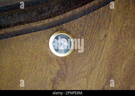 Chiudere il foro sul legno. primo piano, spioncino della lente della porta su tessuto di legno bianco. Occhio della porta, alla porta. Fuori fuoco. Foto Stock