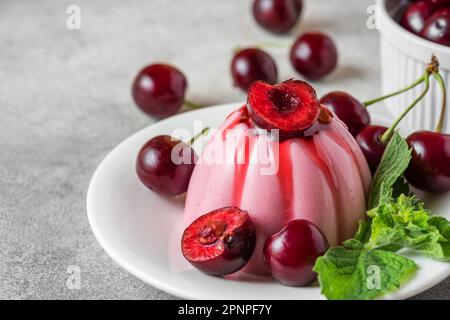 Delizioso dessert di panna cotta alle ciliegie con frutti di bosco freschi, salsa di frutta e menta in un piatto su un tavolo grigio. Cucina italiana. Foto Stock