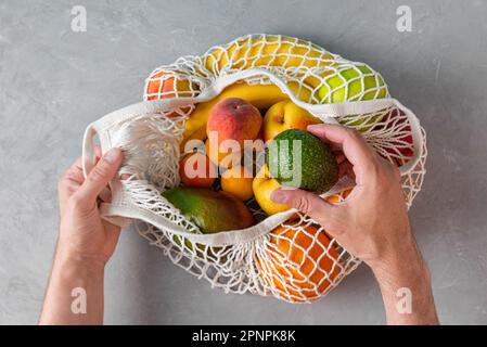 Gli uomini prendono l'avocado dai sacchetti di shopping della maglia con i prodotti biologici della frutta. Shopper eco-friendly in mesh. Concetto senza plastica. Vista dall'alto Foto Stock