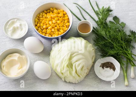 Ingredienti per insalata di cavolo con mais: Cavolo bianco, mais, uova, erbe aromatiche, maionese, panna acida, aceto di sidro di mele, sale, pepe su bac grigio chiaro Foto Stock
