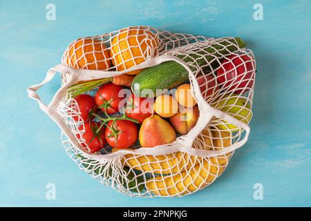 Mesh shopping bag con frutta biologica sana in verdure dal mercato su sfondo blu. Vista dall'alto. Prodotti vegani o vegetariani. Li. Sostenibile Foto Stock