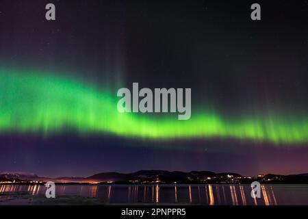 Una splendida vista dell'Aurora boreale che illumina lo skyline della città vicino a un lago di notte Foto Stock