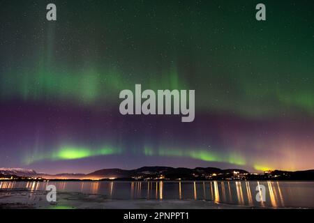 Una splendida vista dell'Aurora boreale che illumina lo skyline della città vicino a un lago di notte Foto Stock