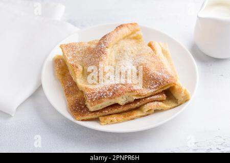 Un piatto di tradizionali pancake finlandesi o danesi pannukakku cosparso di zucchero a velo con panna acida e marmellata su sfondo chiaro. Delizioso ve Foto Stock