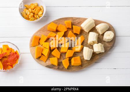 Asse di legno con polpa di zucca e banana tagliata a pezzi, semi di zucca e buccia di zucca. Cucina deliziosa frittelle di zucca banana, vista dall'alto Foto Stock