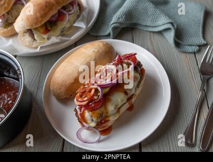 Cheeseburger su baguette francese con formaggio fuso, salsa barbecue, cipolle, pomodori e sottaceti su un piatto aperto Foto Stock