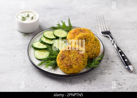 Deliziose cotolette di miglio con carote e semi serviti con cetriolo ed erbe su sfondo grigio. Cibo vegano fatto in casa Foto Stock