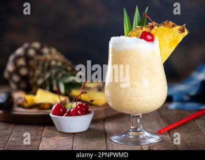 Cocktail Pina colada con ciliegia, fetta di ananas e foglie su sfondo scuro con spazio copia Foto Stock