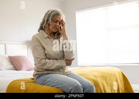 Preoccupata donna caucasica anziana seduta sul letto che tiene la testa Foto Stock