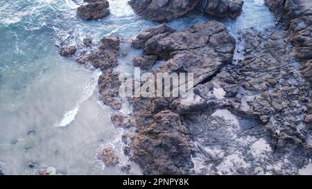 Una splendida vista aerea di una spiaggia incontaminata dell'oceano, caratterizzata da un corpo di acqua blu turchese con onde bianche e una costa rocciosa Foto Stock