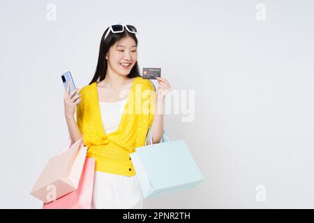 Felice giovane donna che trasporta le borse di shopping con usando la carta di credito ed il telefono mobile che si levano in piedi sopra isolato su fondo bianco. Foto Stock