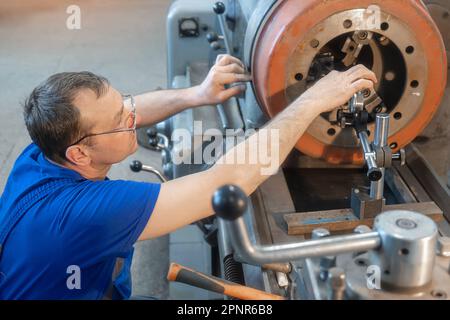 Turner con vetri che lavorano al tornio sul pavimento del negozio. Il Turner allinea il disco del freno del carrello sul tornio. Foto Stock