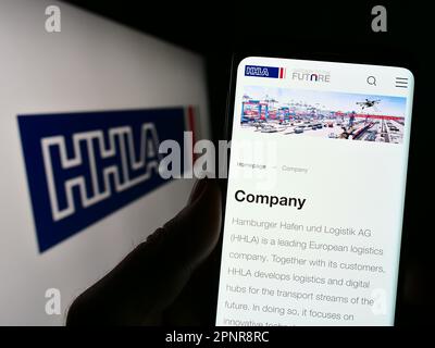 Persona che tiene in mano uno smartphone con la pagina Web della società Hamburger Hafen und Logistik AG (HHLA) sullo schermo con il logo. Messa a fuoco al centro del display del telefono. Foto Stock