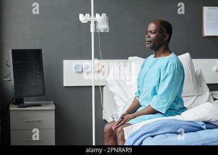 Uomo anziano afroamericano con contagocce seduto sul letto nel reparto dell'ospedale Foto Stock