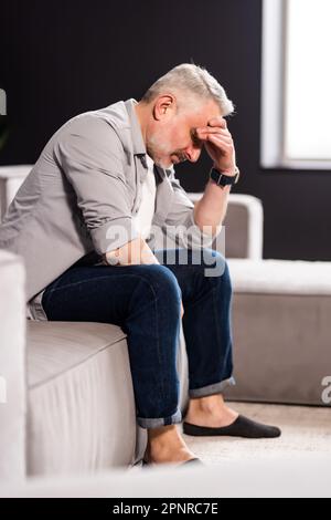 Frustrato uomo di mezza età seduto sul divano a casa. Primo piano faccia di un uomo d'affari stressato che indossa gli occhiali con gli occhi chiusi. Iperlavorato medio-est Foto Stock