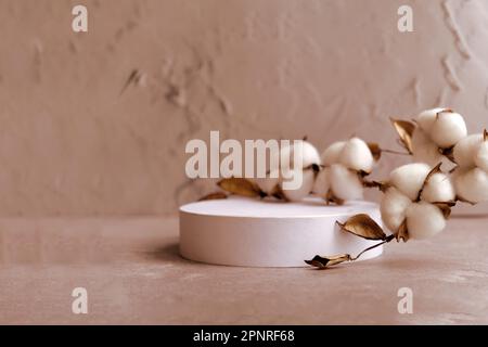 podio rotondo bianco con ramo di cotone su fondo naturale beige. Mockup per promuovere prodotti ecologici o biologici , cosmetici. Foto Stock