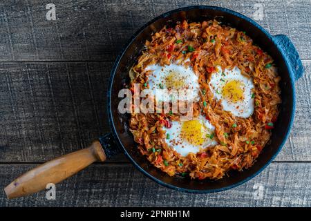 Cavolo stufato con verdure e uova fritte in una padella su uno sfondo di legno, primo piano, vista dall'alto. Cibo sfondo. Cibo sano Foto Stock