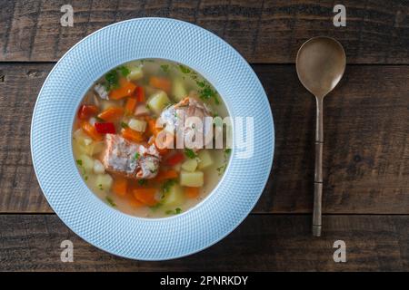 Zuppa di salmone fresco con carote, patate e peperoni rossi in un piatto bianco su tavolo di legno, primo piano. La cena gustosa consiste in una zuppa di pesce con sa Foto Stock