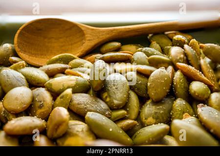 Semi di zucca in una ciotola con un cucchiaio di legno. Primo piano. Foto Stock