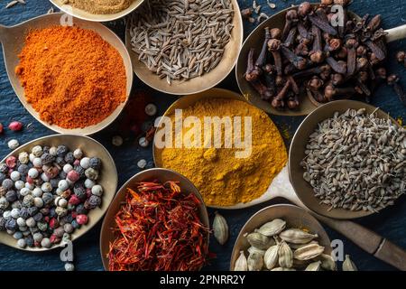 Set di spezie in cucchiai di ottone, primo piano, vista dall'alto. Vari peperoni, cardamomo, garofano, curcuma, paprika e zafferano per cucinare Foto Stock