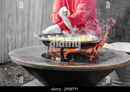 Le verdure sono tostate su un focolare rotondo. Griglia rotonda a forma di ciotola con un fuoco all'interno. L'uomo prepara il focolare per il barbecue. La legna da ardere sta bruciando Foto Stock