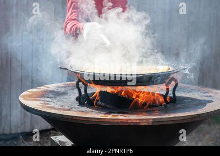 Le verdure sono tostate su un focolare rotondo. Griglia rotonda a forma di ciotola con un fuoco all'interno. L'uomo prepara il focolare per il barbecue. La legna da ardere sta bruciando Foto Stock