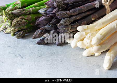 Asparagi crudi bianco, viola, verde su sfondo blu. Concetto di cibo crudo, luogo per spazio di copia. Foto Stock