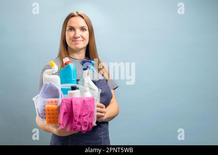 Donna che tiene un contenitore con un set di prodotti per la pulizia su sfondo blu Foto Stock