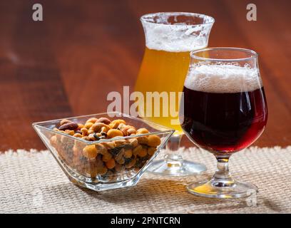 Bicchieri di birra belga bionda gialla e bruna scura preparati in abbazia serviti al bar con noci da festa, primo piano Foto Stock