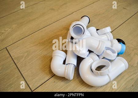 Tubazioni in plastica bianca, tubi idraulici, lisci e curvi, raccordi, flange, guarnizioni in gomma. Sullo sfondo di tavole beige. Foto Stock