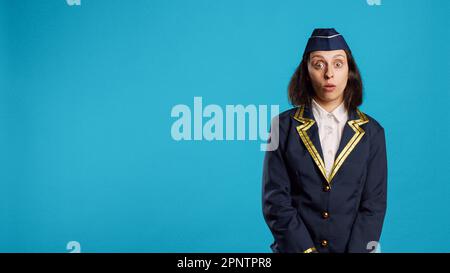 Astuta caucasica dopo aver sorpreso la reazione, essere in shock dopo aver sentito notizie sulla fotocamera. Giovane donna vestita come hostess aria sensazione stupito e stupito in studio, scioccato aereo di linea. Foto Stock