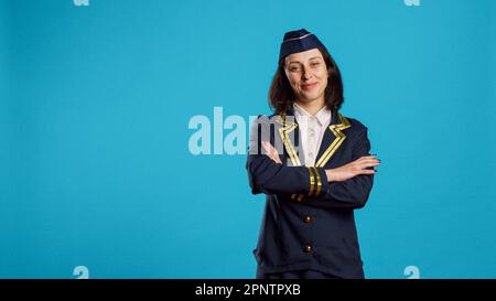 Giovane donna sorridente che lavora come hostess dell'aria, che indossa l'uniforme volante e che si posa con fiducia. Allegra machessa che si prepara per il volo commerciale, che lavora nel settore dell'aviazione. Foto Stock