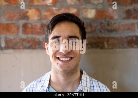 Ritratto di uomo d'affari casual caucasico felice sorridendo contro muro di mattoni in ufficio Foto Stock