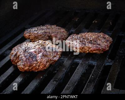 La classica semplicità di tre hamburger semplici, cucinati alla perfezione su una griglia per una cucina estiva. Le polpette di manzo sono succose e saporite, senza nulla Foto Stock